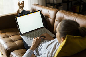 Young woman lying on couch at home using laptop - GIOF06722