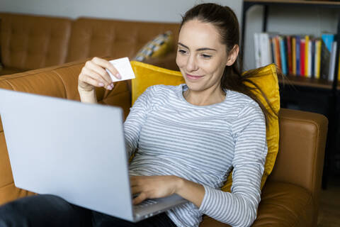 Young woman on couch at home shopping online stock photo