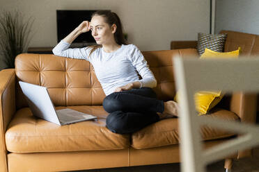 Young woman sitting on couch at home with laptop - GIOF06726