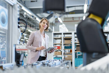 Businesswoman with tablet in a modern factory hall looking at robot - DIGF07211