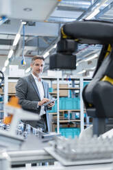 Businessman with tablet in a modern factory hall looking at robot - DIGF07213