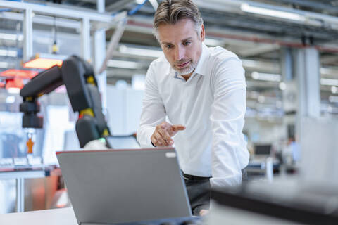 Geschäftsmann in einer modernen Fabrikhalle mit Laptop, lizenzfreies Stockfoto