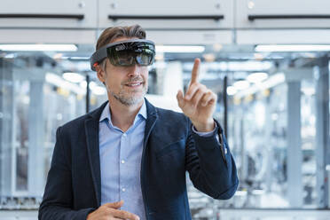 Businessman wearing AR glasses in a modern factory - DIGF07237