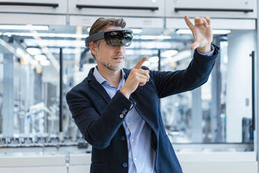 Businessman wearing AR glasses in a modern factory - DIGF07241