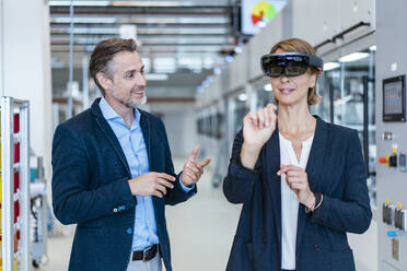 Businesswoman with AR glasses and businessman in a modern factory - DIGF07253