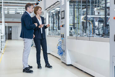 Businessman and businesswoman looking at a machine in a modern factory hall - DIGF07261