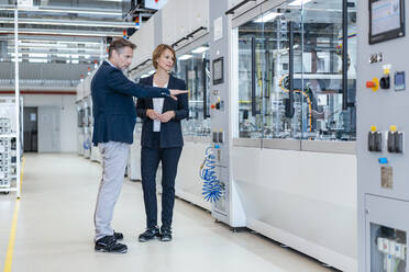 Businessman and businesswoman looking at a machine in a modern factory hall - DIGF07262