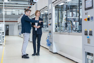 Geschäftsmann und Geschäftsfrau betrachten eine Maschine in einer modernen Fabrikhalle - DIGF07262