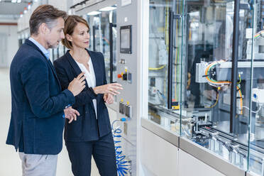 Businessman and businesswoman looking at a machine in a modern factory hall - DIGF07266