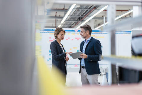 Geschäftsmann und Geschäftsfrau im Gespräch in einer Fabrikhalle, lizenzfreies Stockfoto