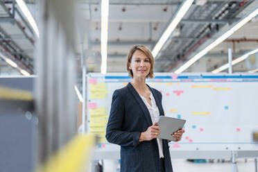 Portrait of confident businesswoman with tablet in a factory hall - DIGF07279