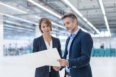 Businessman and businesswoman discussing plan in a factory hall - DIGF07280