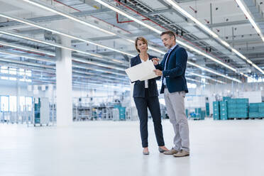 Businessman and businesswoman discussing plan in a factory hall - DIGF07282