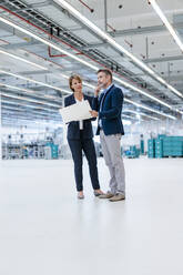 Businessman and businesswoman discussing plan in a factory hall - DIGF07283