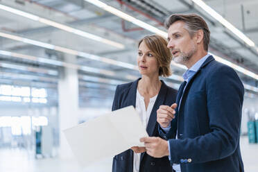 Businessman and businesswoman discussing plan in a factory hall - DIGF07284