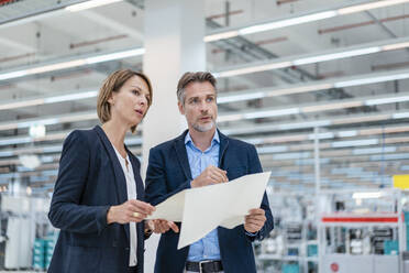 Businessman and businesswoman discussing plan in a factory hall - DIGF07286