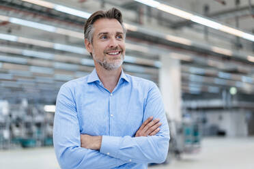 Portrait of a smiling businessman in a factory hall - DIGF07296