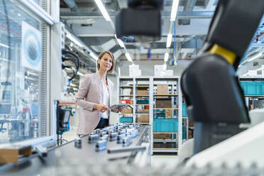 Businesswoman with tablet in a modern factory hall looking at robot - DIGF07301