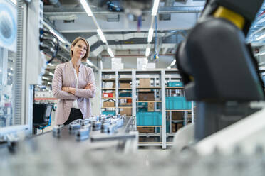 Geschäftsfrau in einer modernen Fabrikhalle mit Blick auf einen Roboter - DIGF07302