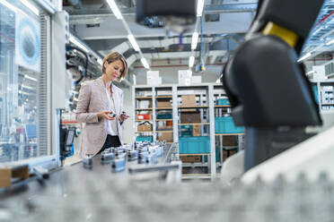 Businesswoman examining workpieces in a modern factory hall - DIGF07304