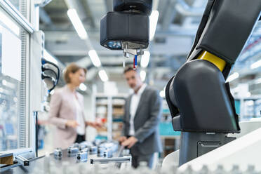 Robot in a modern factory hall with businessman and businesswoman in background - DIGF07306