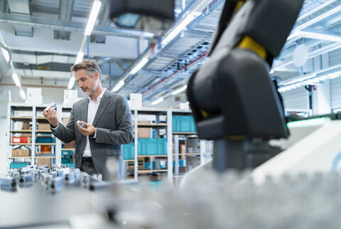 Geschäftsmann bei der Prüfung von Werkstücken in einer modernen Fabrikhalle, lizenzfreies Stockfoto