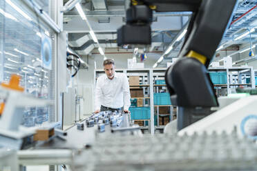 Businessman in a modern factory hall looking at robot - DIGF07310