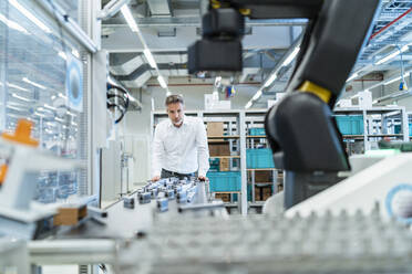 Geschäftsmann in einer modernen Fabrikhalle mit Blick auf einen Roboter - DIGF07310