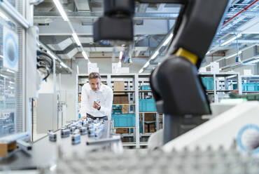 Geschäftsmann in einer modernen Fabrikhalle mit Blick auf einen Roboter - DIGF07311