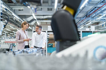 Businessman and businesswoman talking in a modern factory hall - DIGF07317