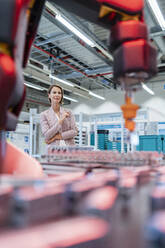 Businesswoman in a modern factory hall looking at robot - DIGF07322
