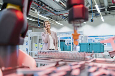 Businesswoman on cell phone in a modern factory hall - DIGF07323