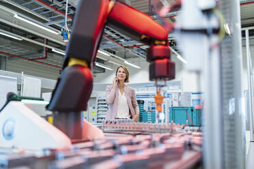 Businesswoman on cell phone in a modern factory hall - DIGF07324