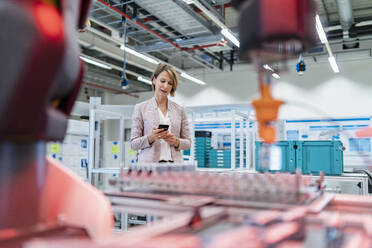 Businesswoman using cell phone in a modern factory hall - DIGF07325