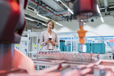 Geschäftsfrau benutzt Mobiltelefon in einer modernen Fabrikhalle - DIGF07325