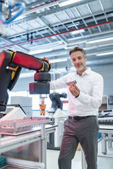 Confident businessman holding workpiece in a modern factory hall - DIGF07328