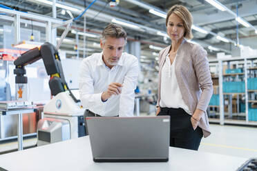 Geschäftsmann und Geschäftsfrau mit Laptop im Gespräch in einer modernen Fabrikhalle - DIGF07339