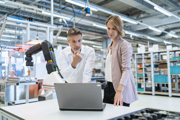 Geschäftsmann und Geschäftsfrau mit Laptop im Gespräch in einer modernen Fabrikhalle - DIGF07340