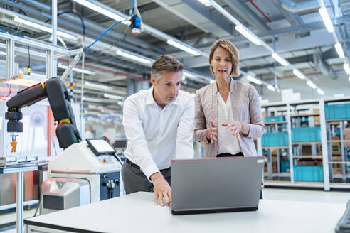 Businessman and businesswoman with laptop talking in a modern factory hall - DIGF07341