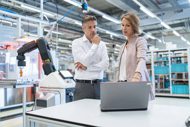 Businessman and businesswoman with laptop talking in a modern factory hall - DIGF07342