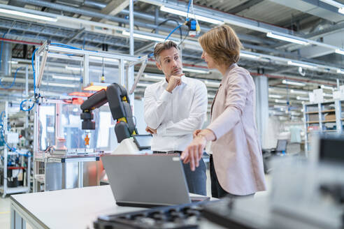 Geschäftsmann und Geschäftsfrau mit Laptop im Gespräch in einer modernen Fabrikhalle - DIGF07344