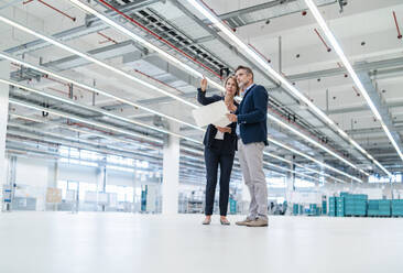 Businessman and businesswoman discussing plan in a factory hall - DIGF07352