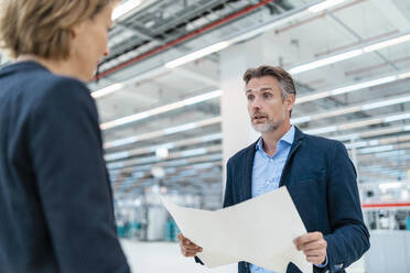 Businessman and businesswoman discussing plan in a factory hall - DIGF07356