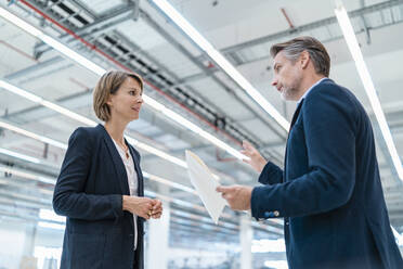 Geschäftsmann und Geschäftsfrau besprechen einen Plan in einer Fabrikhalle - DIGF07357