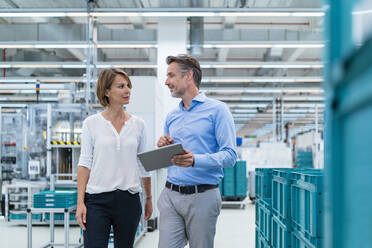 Businessman and businesswoman with tablet talking in a factory hall - DIGF07373