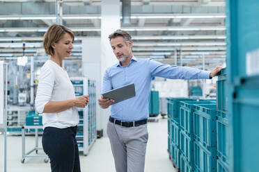 Businessman and businesswoman with tablet talking in a factory hall - DIGF07374