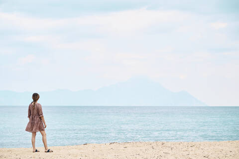 Griechenland, Rückansicht einer Frau mit Blick auf den Berg Athos über das Meer, lizenzfreies Stockfoto