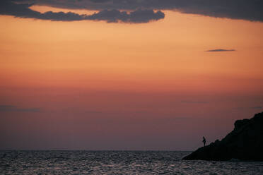 Silhouette of person fishing in sea at sunrise - BZF00494