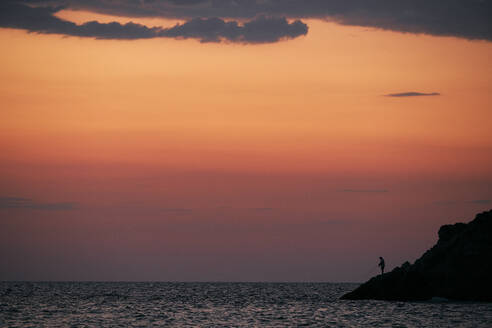 Silhouette einer Person, die bei Sonnenaufgang im Meer fischt - BZF00494