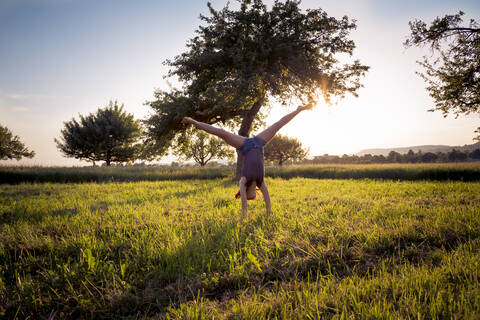 Teenager-Mädchen macht Handstand in grasbewachsenen Feld bei Sonnenuntergang, lizenzfreies Stockfoto